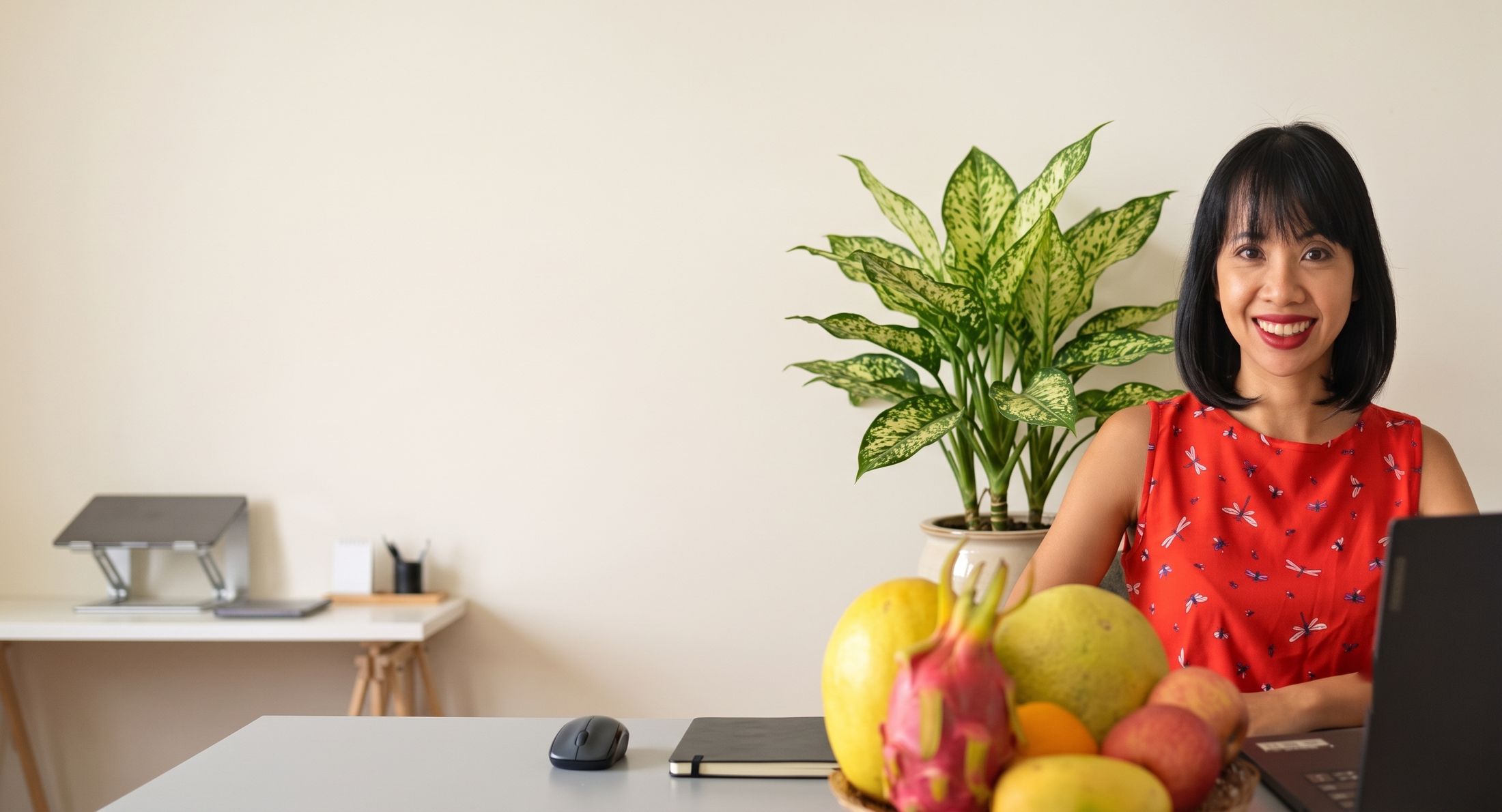 Elizabeth smiling at her desk with a bowl of fresh fruit and a plant